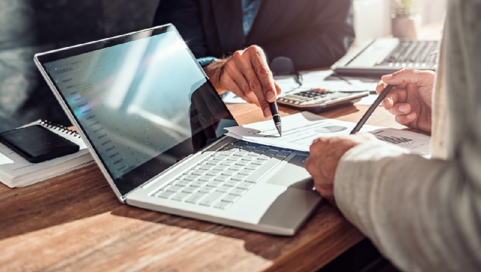 Two people reviewing financial documents at a wooden desk with a laptop and calculator, suggesting a professional compensation discussion or negotiation meeting