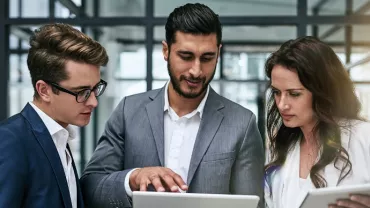 Three business professionals reviewing documents on tablets.