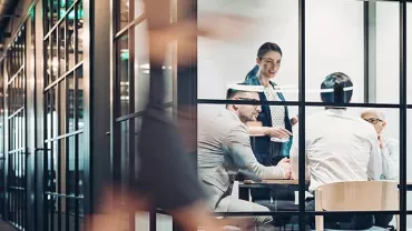 People in a modern glass-walled office having a meeting.