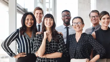 Group of seven people smiling in a bright office setting.