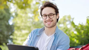 Smiling person with glasses sitting outside on a sunny day