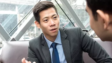 Two men in business attire having a conversation in a modern office setting.