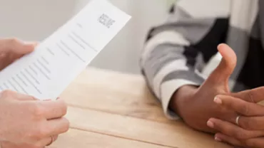 Two people at a table during a job interview, one holding a resume.