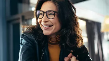 Smiling woman in glasses sits at a table indoors.