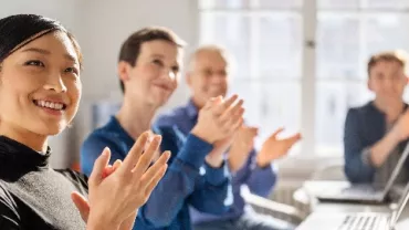 A group of colleagues smiling and clapping in an office meeting.