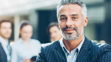 Confident man in a suit with colleagues in the background.